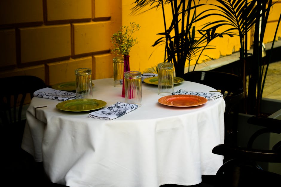 A beautifully set round dining table with colorful plates and glasses, perfect for outdoor dining.